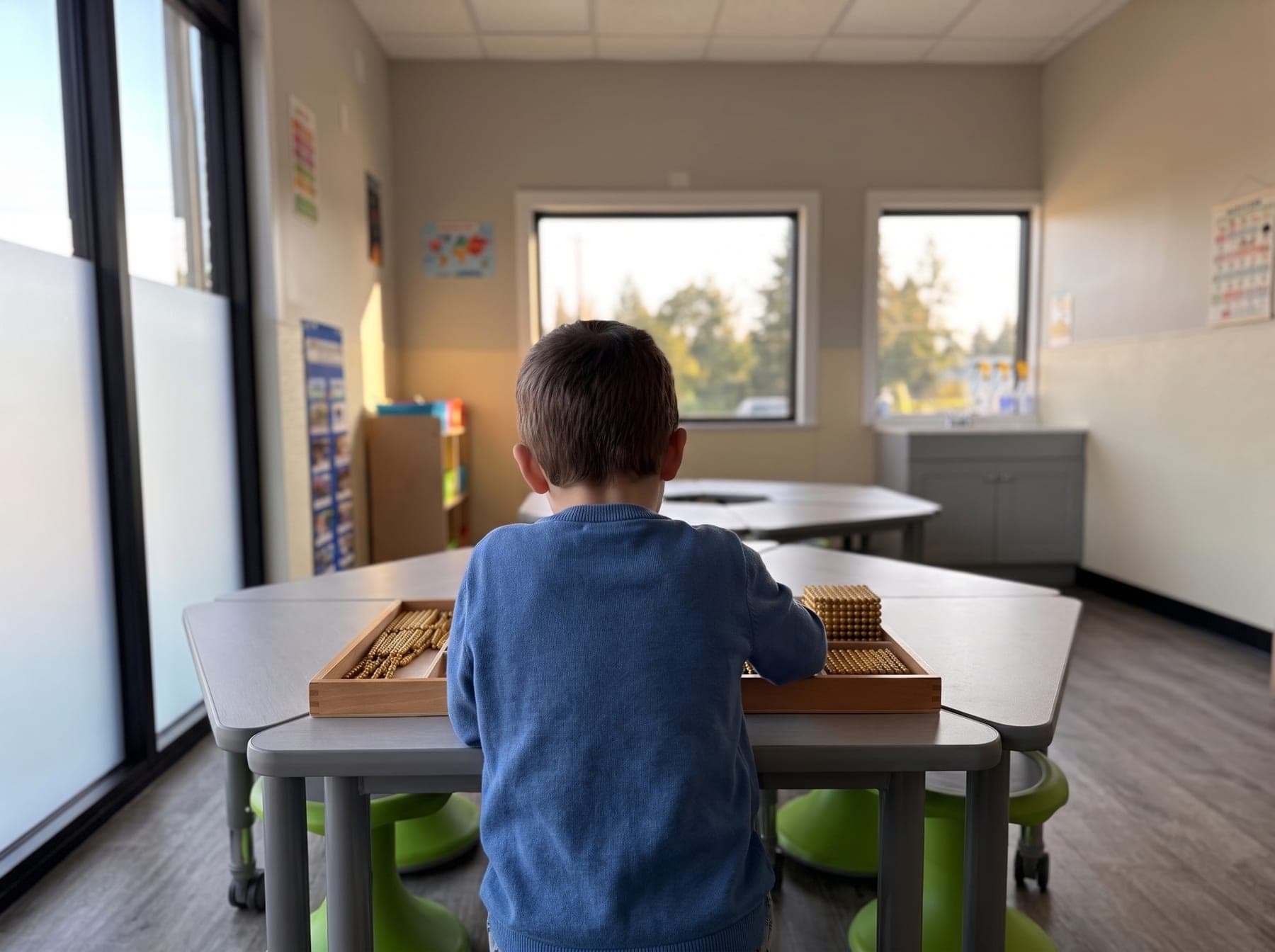 A child, seen from behind, working with golden bead material in window light