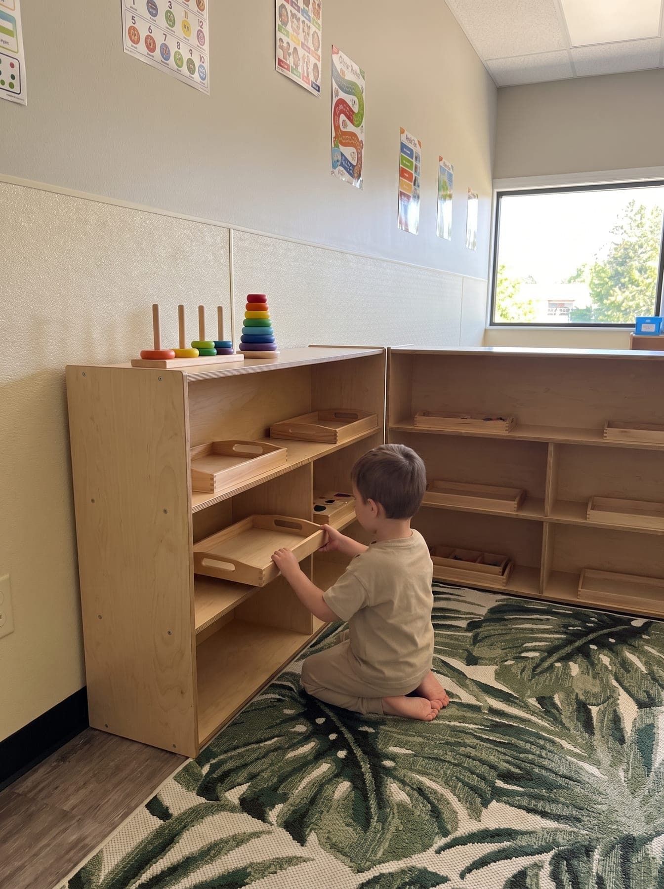 A child, seen from behind, lifting a wooden tray from a low birch shelf