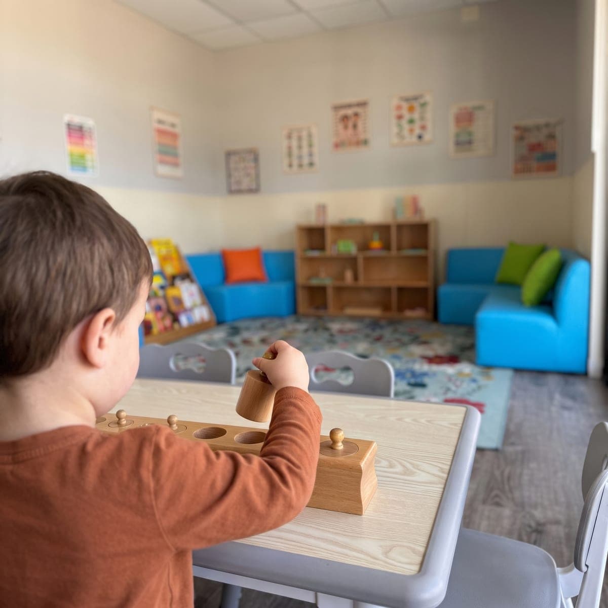 Over a child's shoulder: small fingers lifting a knobbed cylinder from its block at a low table