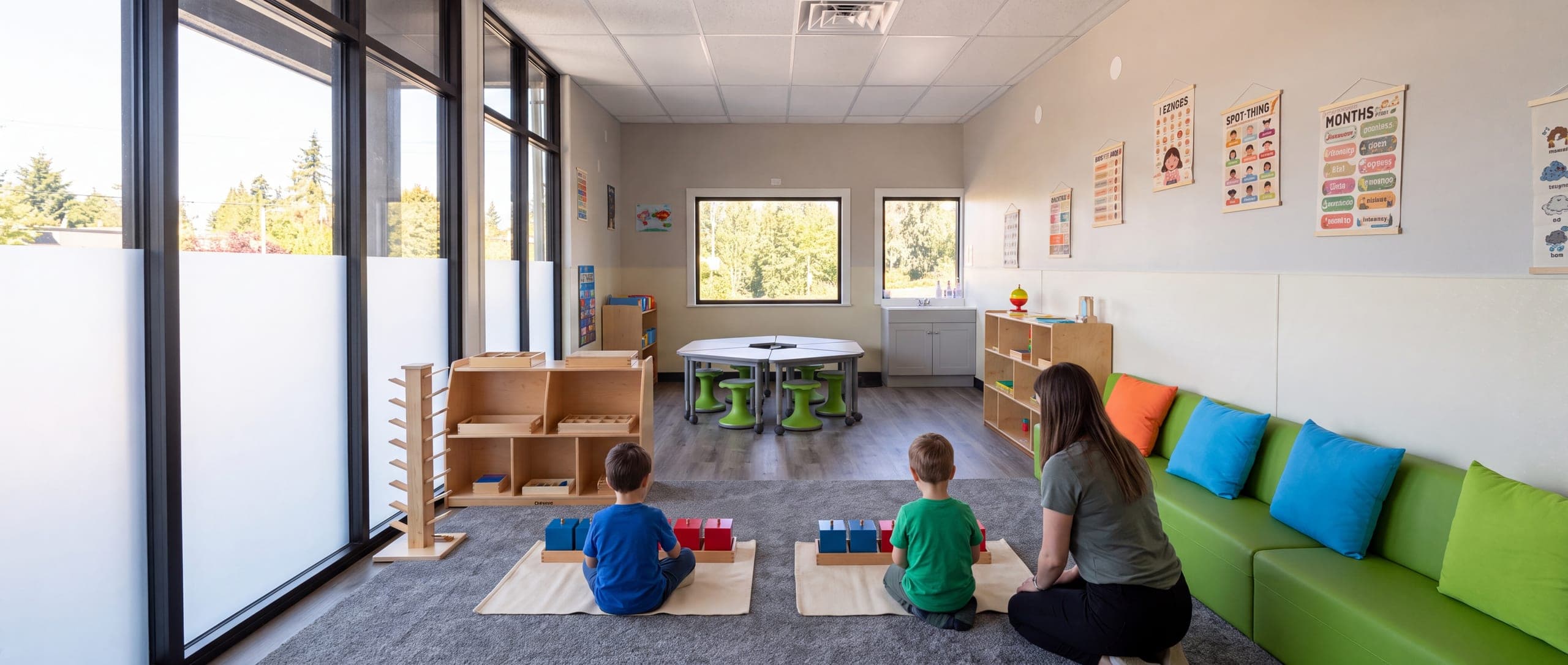 A classroom during the work cycle, children seen from behind at their mats along the window wall