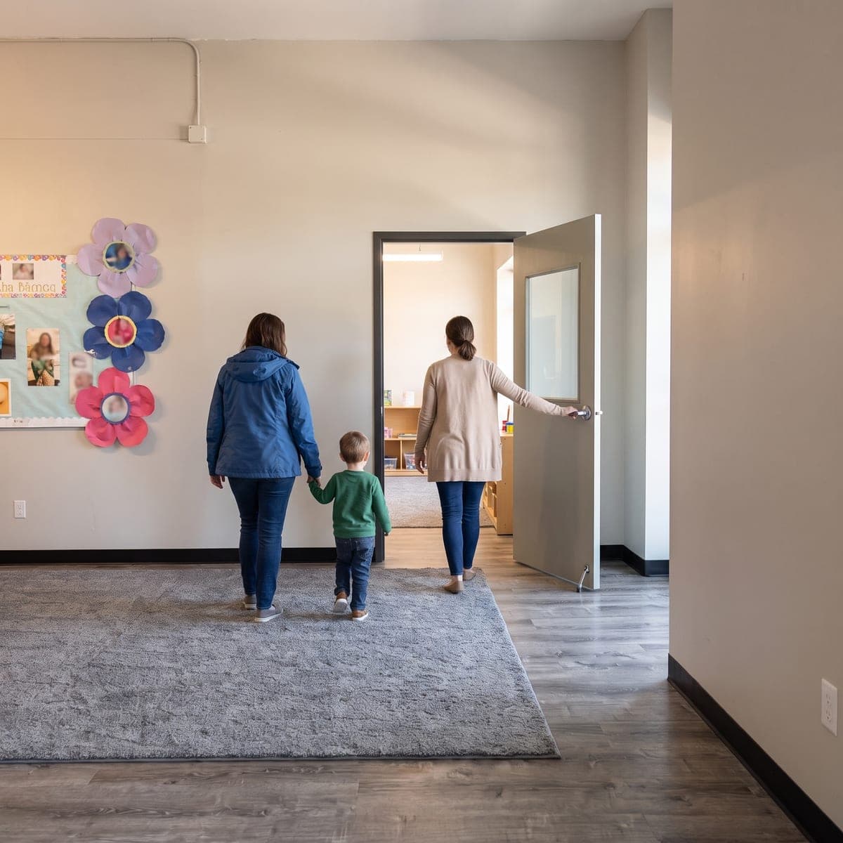 From behind: a parent and child walk hand in hand across the lobby toward the open glazed door, where a guide holds it open