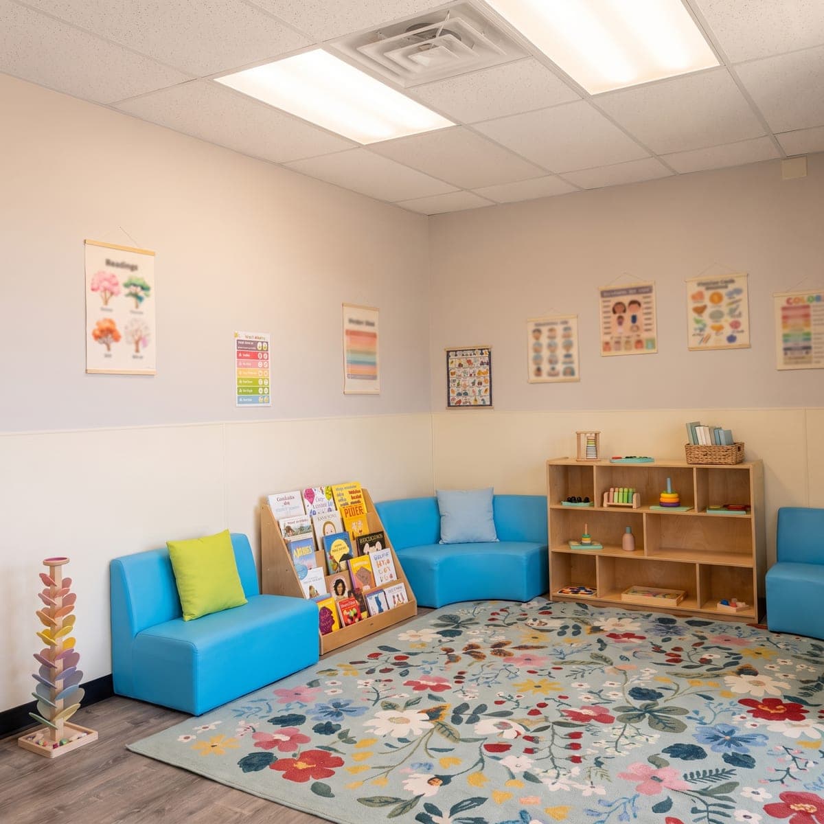 The reading nook: picture books facing out on a birch stand, a small armchair and the floral rug