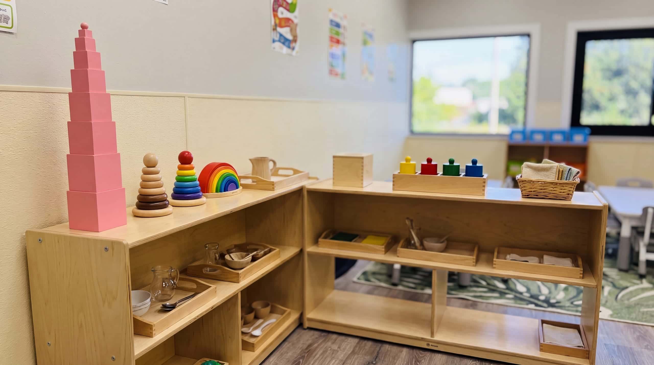 A low birch shelf lined with wooden trays of Montessori materials in soft light